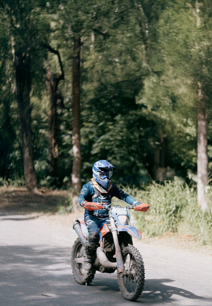 ALT_TEXT: Motorcyclist with gear rides on a dirt path in a forested area.