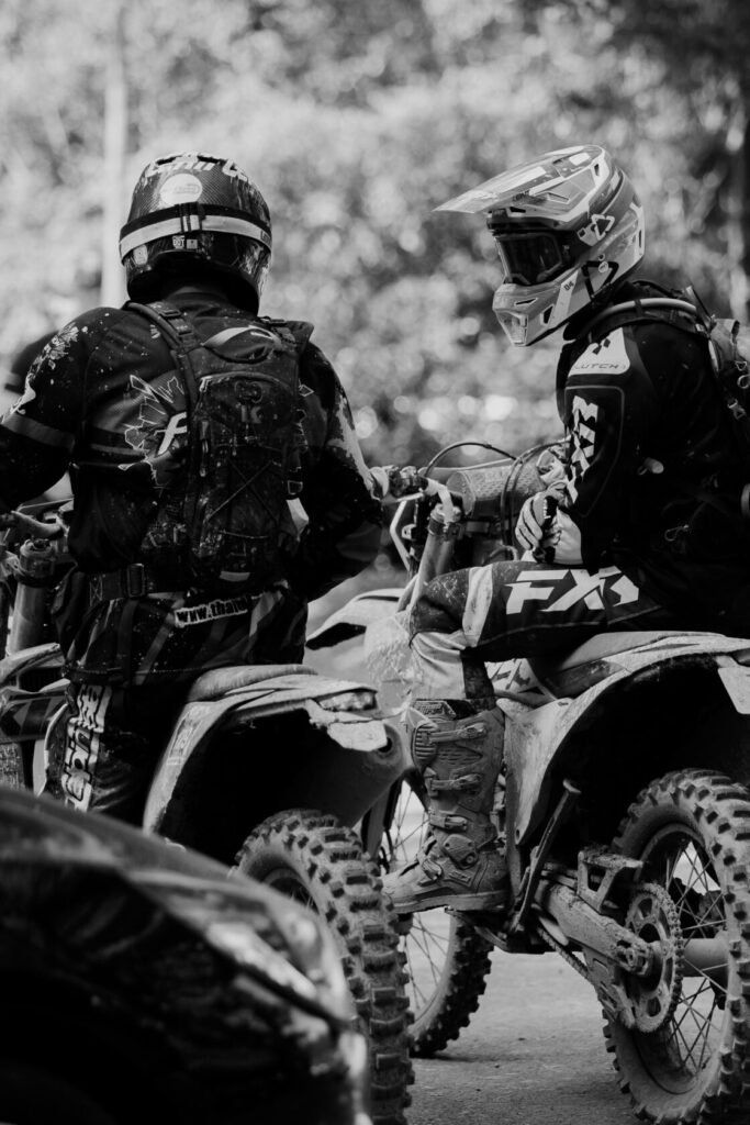 ALT_TEXT: Two motocross riders on dirt bikes, wearing gear and helmets, converse in a forest setting.

CAPTION_TEXT: In a peaceful forest se