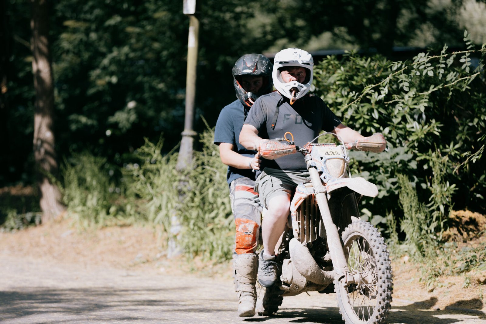 ALT_TEXT: Two people wearing helmets riding a motorbike in a wooded area.