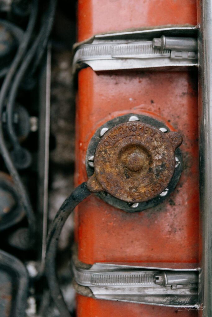 Close-up of a rusty engine cap on a red engine component, with a metal clamp and electrical wiring visible.