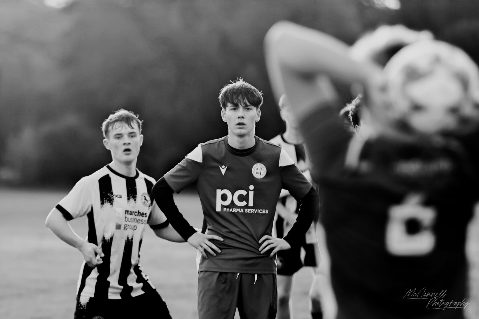 Two young football players on the pitch during a match. One player is wearing a red jersey with 'pci' on it, looking focused, while another player in a black and white striped shirt appears surprised.