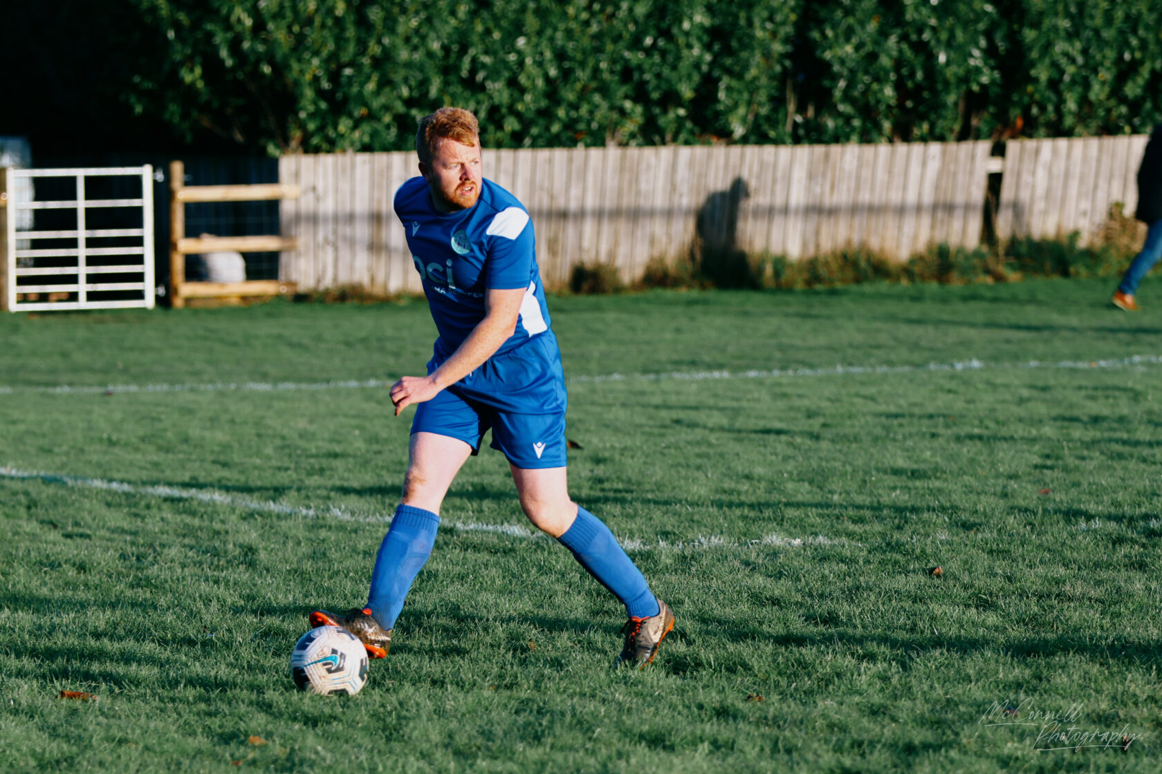 A player in a blue football kit is preparing to kick a ball on a grassy football pitch.