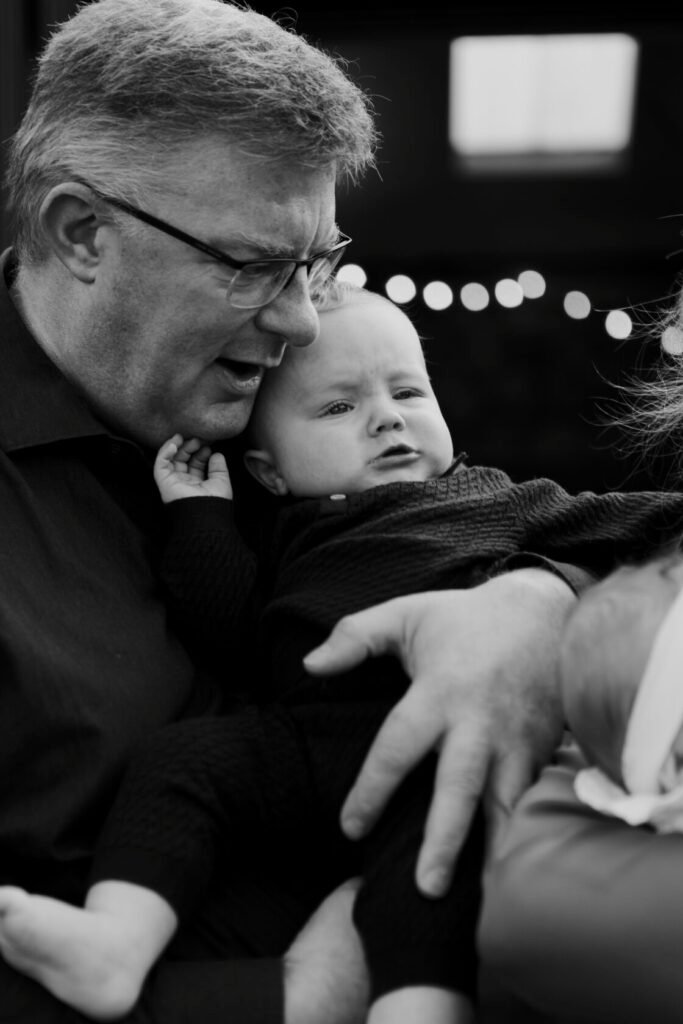 A man with glasses embraces a baby, both displaying strong emotions. The man appears animated, while the baby looks curious.