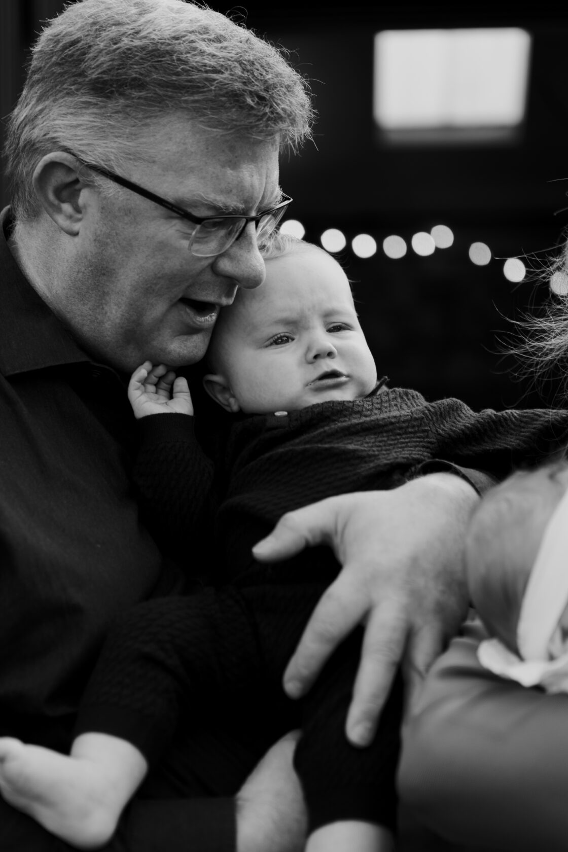 A man with glasses embraces a baby, both displaying strong emotions. The man appears animated, while the baby looks curious.