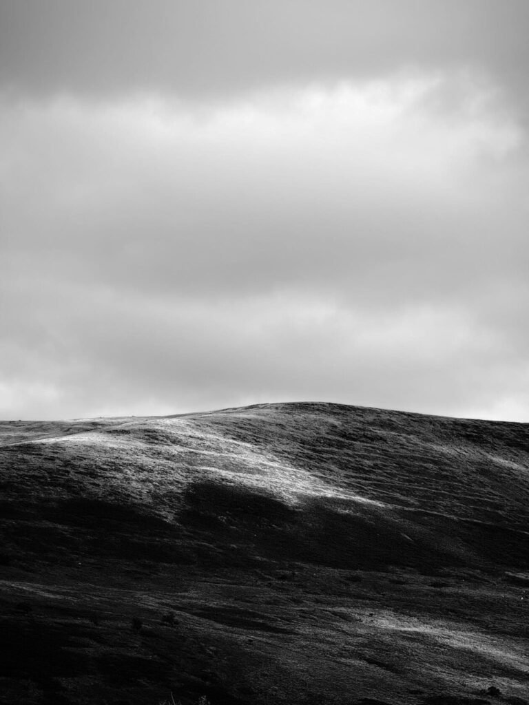 A monochrome landscape featuring rolling hills under a cloudy sky, highlighting various shades of grey and textures in the terrain.