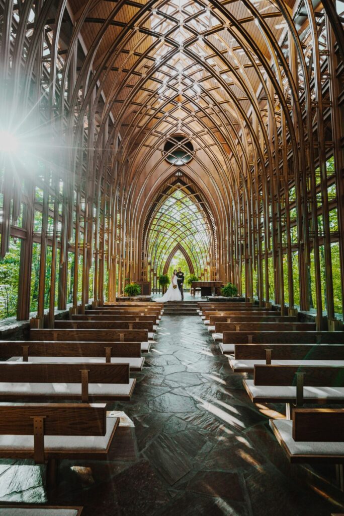 Elegant interior of a chapel featuring intricate wooden arches, natural light streaming through large windows, and empty wooden pews lined up along a stone pathway.