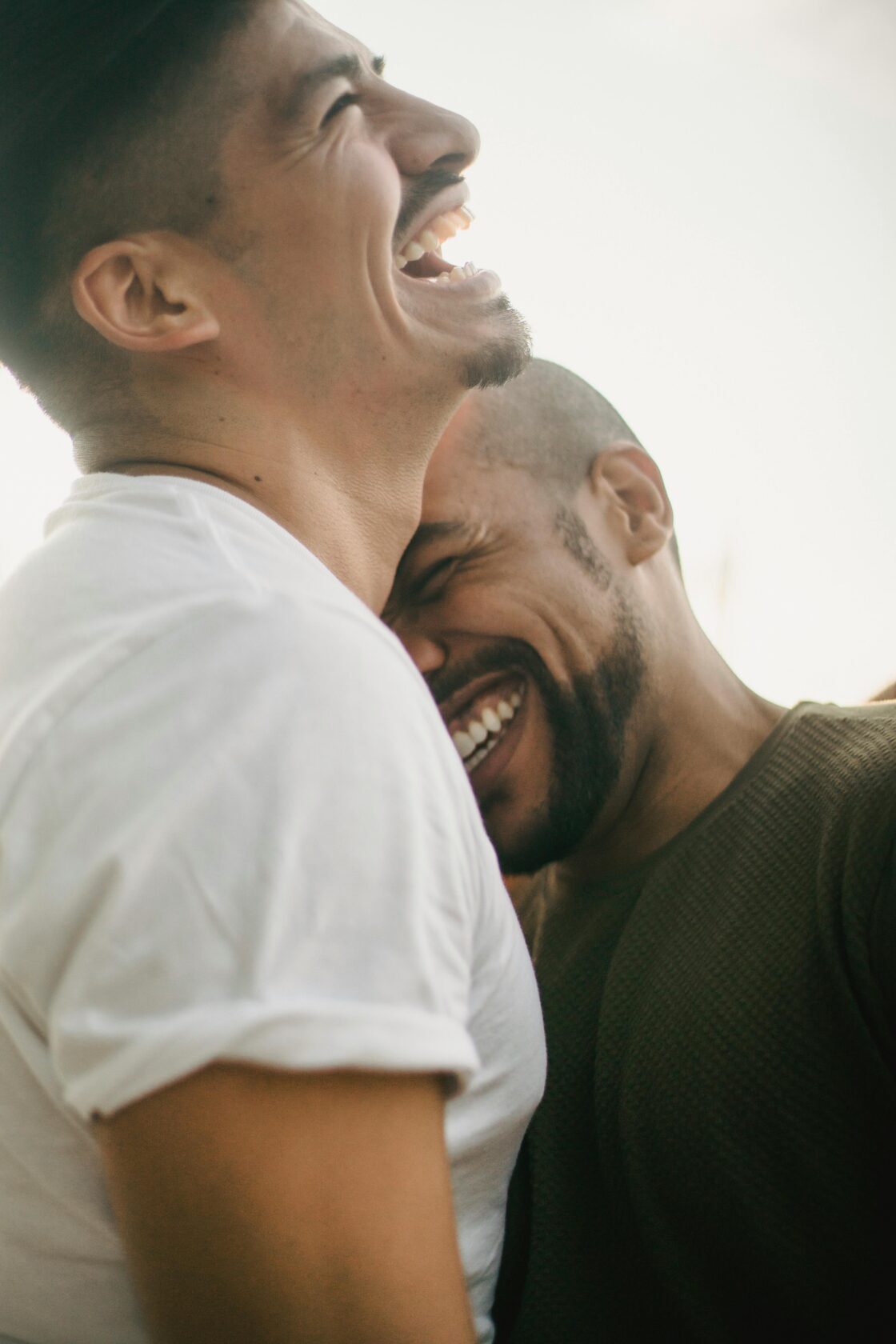 Two men sharing a joyful moment, laughing and embracing each other outdoors, with soft lighting in the background.