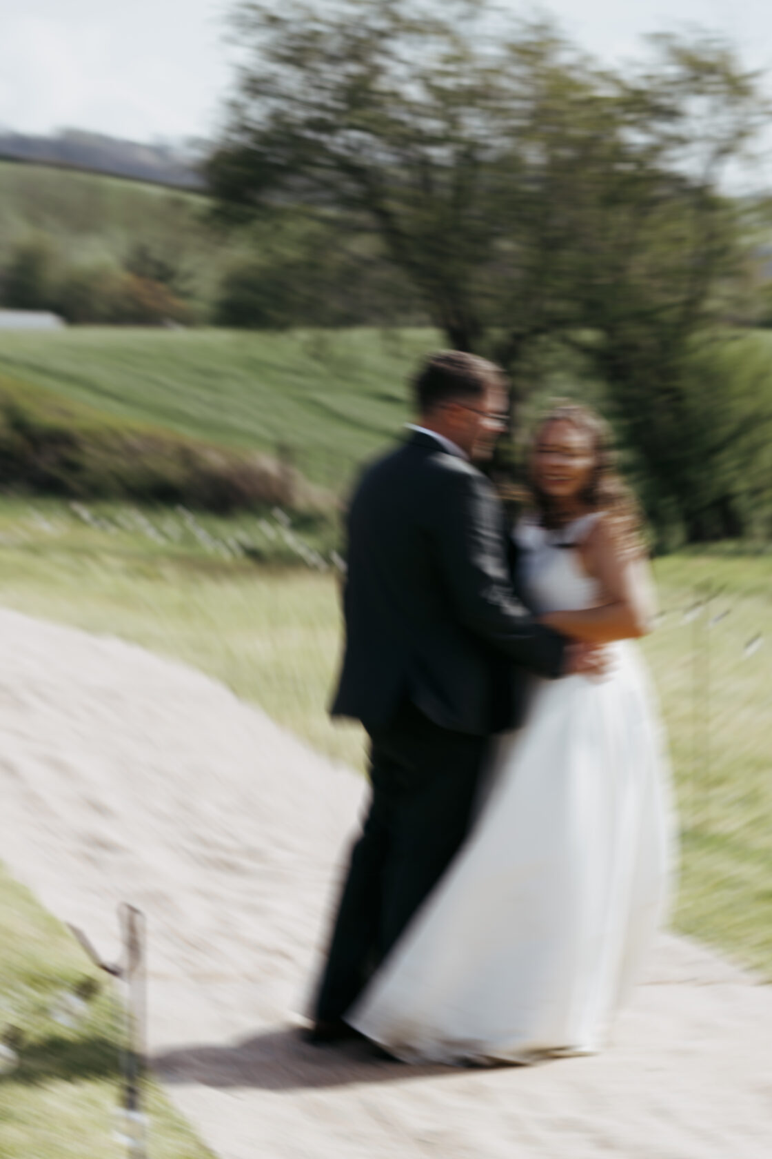A couple embracing on a sandy path during their wedding ceremony, with blurred details of the greenery surrounding them. Shot for Lydia Turner.