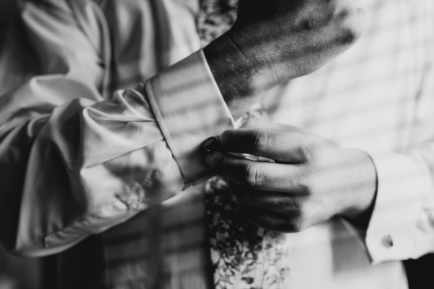 A close-up of a man's hands buttoning his shirt cuff while preparing for a special occasion, featuring a patterned tie. Shot for Lydia Turner.