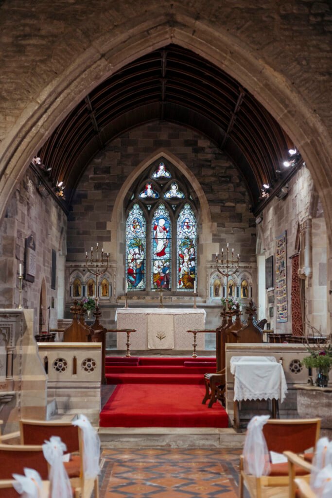 Interior view of a church featuring an ornate altar, bright red carpet, and stunning stained glass windows depicting biblical scenes.
