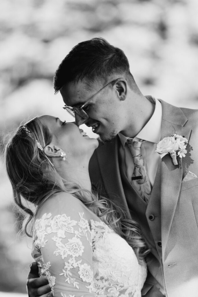 A couple in a romantic embrace, smiling and touching noses, captured in black and white at their wedding.