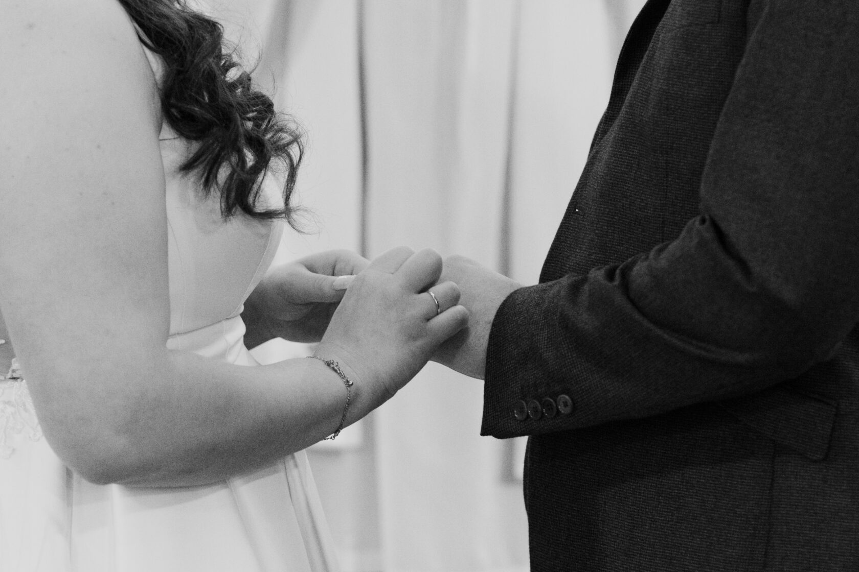 Close-up of a couple holding hands during a wedding ceremony, showcasing the bride's elegant dress and a wedding band on one finger. Shot for Lydia Turner.