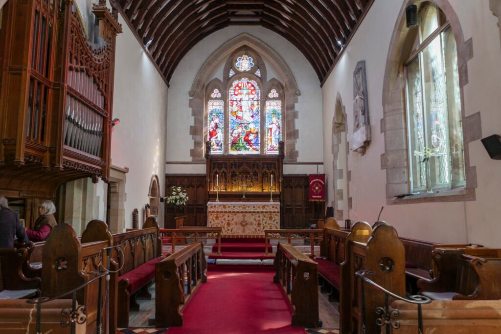 Inside a church featuring wooden pews, a red carpet, a beautifully decorated altar, and colourful stained glass windows depicting biblical scenes. Shot for Lydia Turner.