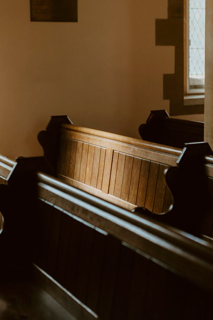 A quiet section of a church interior featuring wooden pews bathed in warm light. The light highlights the natural wood grain, creating a tranquil ambiance. Shot for Lydia Turner.