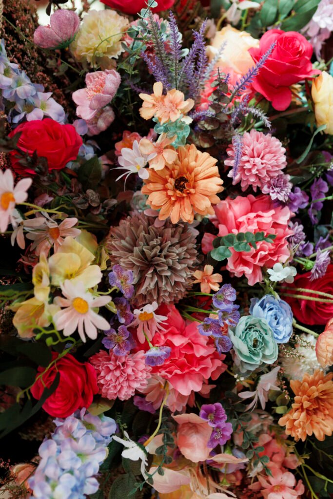A rich and colourful assortment of artificial flowers, including red roses, daisies, and purple blooms, creating an eye-catching display. Shot for Lydia Turner.