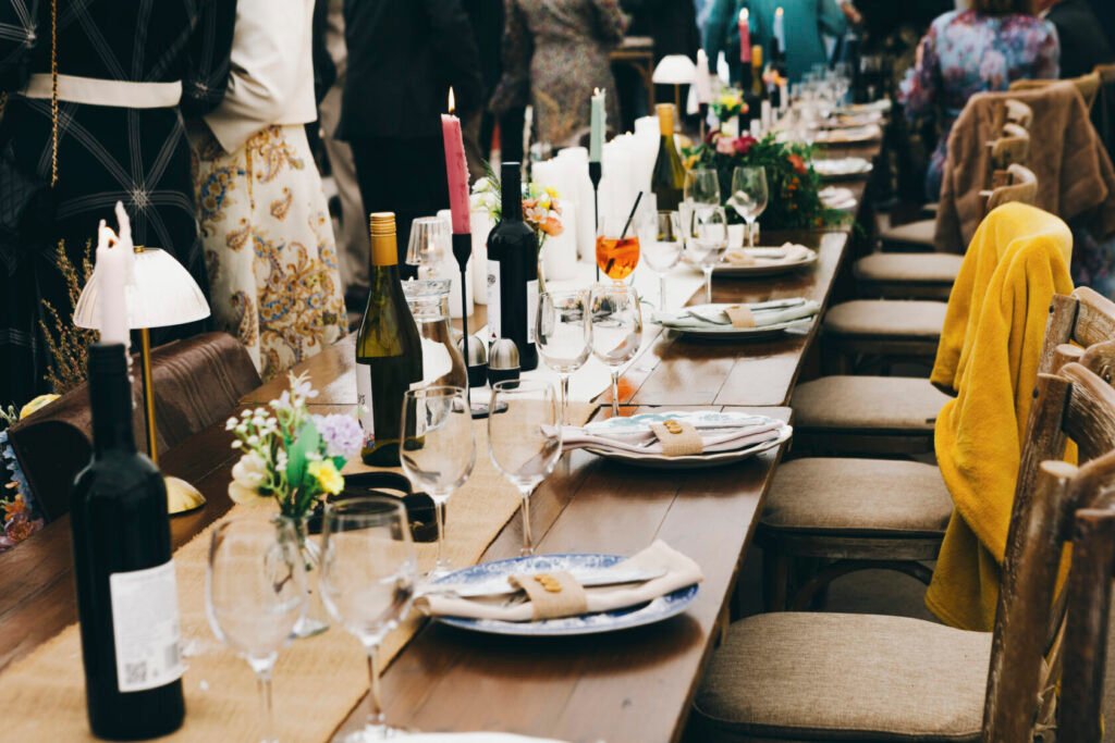 An outdoor dining table elegantly set with wine bottles, glasses, and floral arrangements. Candles and stylish napkins are placed at each seat, creating a festive atmosphere. Shot for Lydia Turner.
