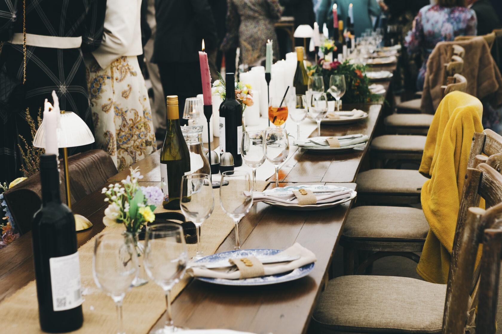 An outdoor dining table elegantly set with wine bottles, glasses, and floral arrangements. Candles and stylish napkins are placed at each seat, creating a festive atmosphere. Shot for Lydia Turner.