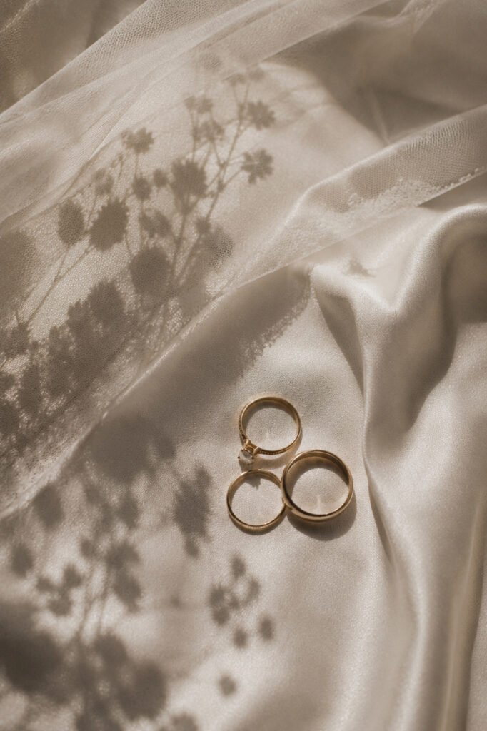 Three gold wedding rings laid on soft satin fabric, with delicate floral shadows cast upon them. Shot for Lydia Turner