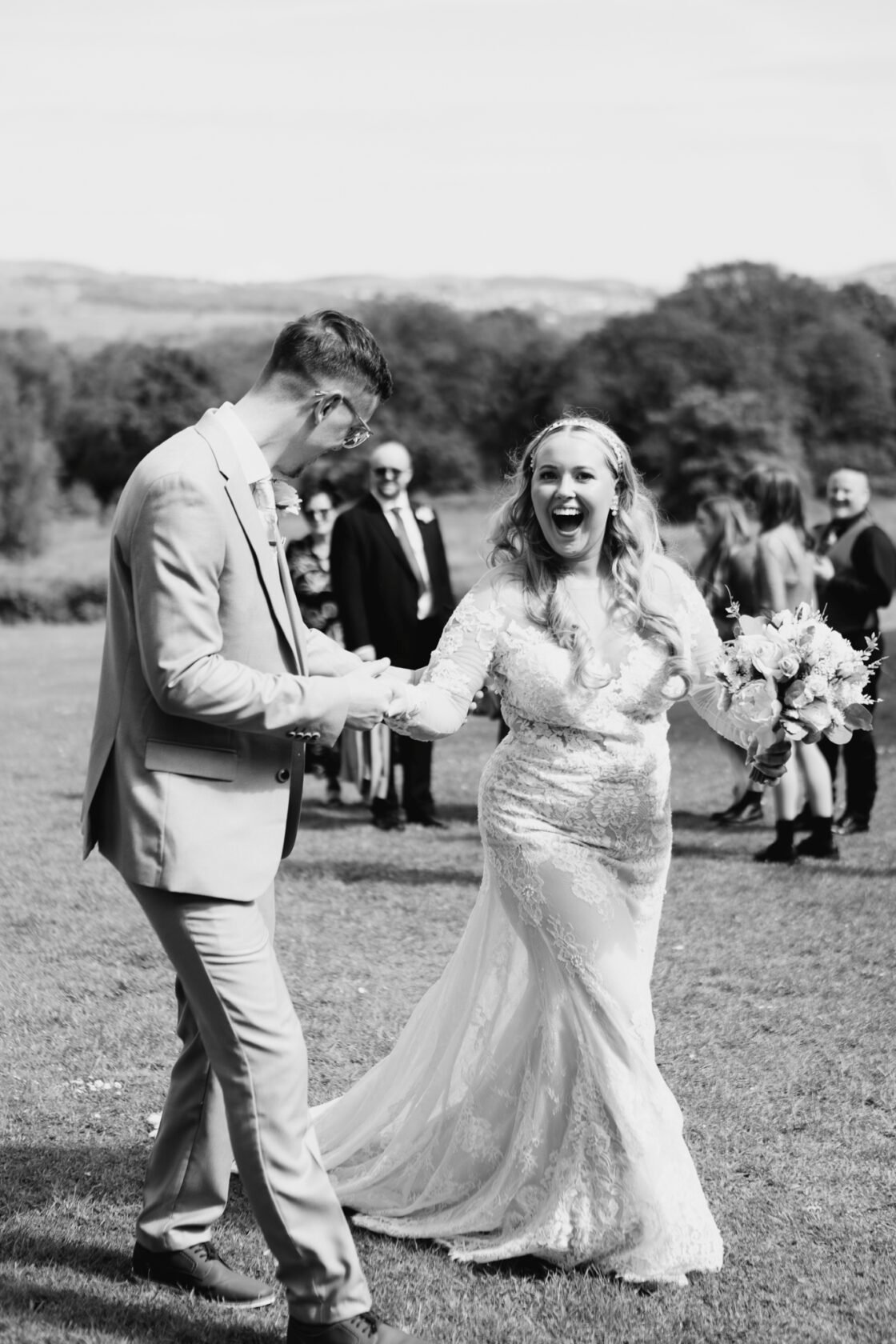 Joyful Wedding Dance Bride in a detailed lace wedding dress joyfully dancing with her partner in a grassy field, surrounded by wedding guests.