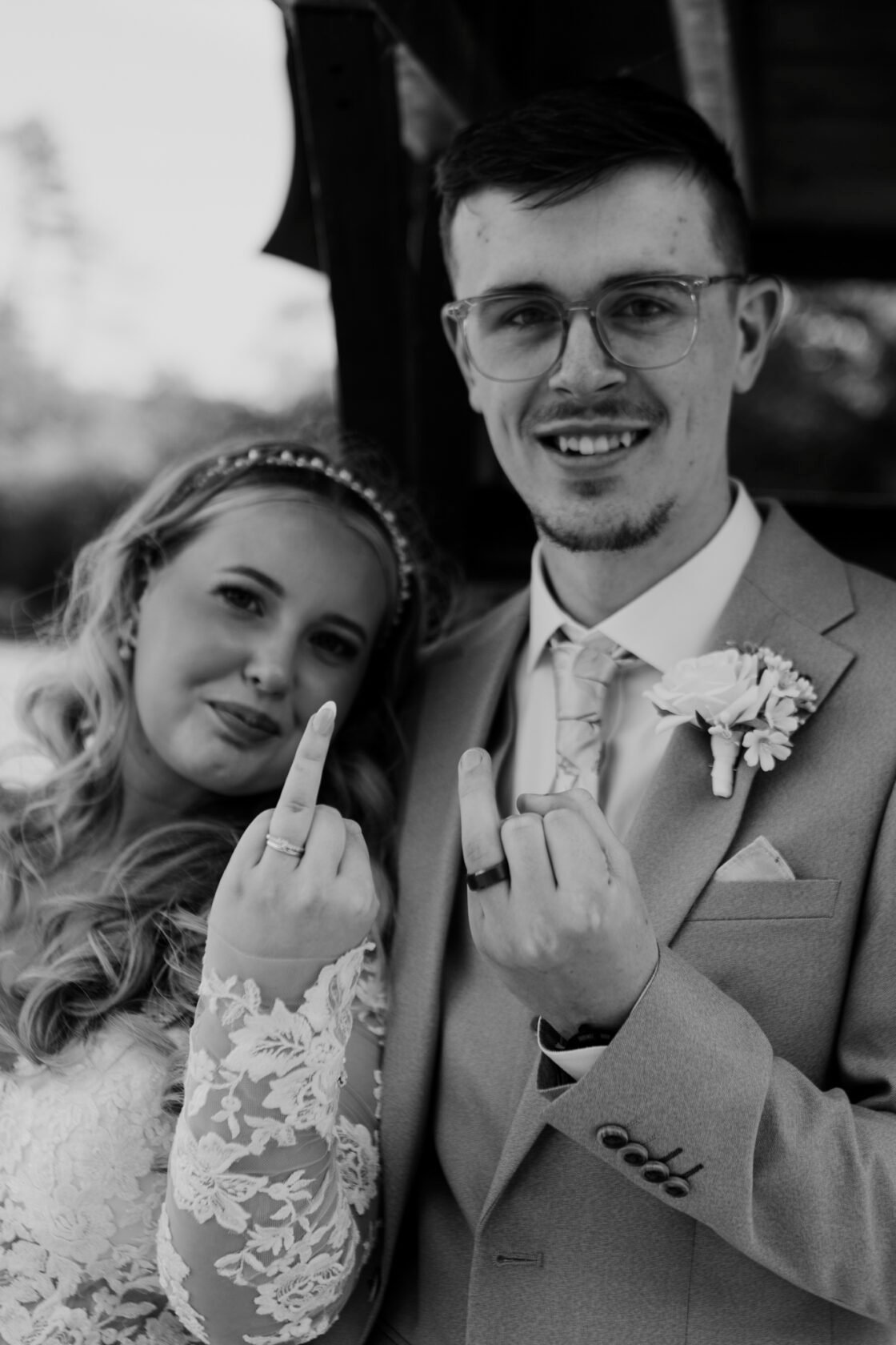 Playful Wedding Portrait with Couple Black and white portrait of a smiling bride and groom, both showing their wedding rings and making playful gestures with their fingers.