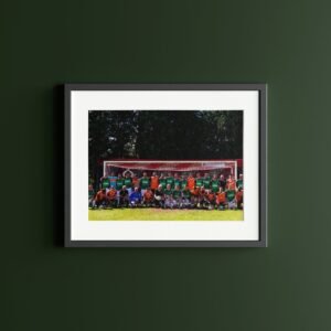 Group photo of a football team standing on grass in front of a goal post, wearing green and orange jerseys.