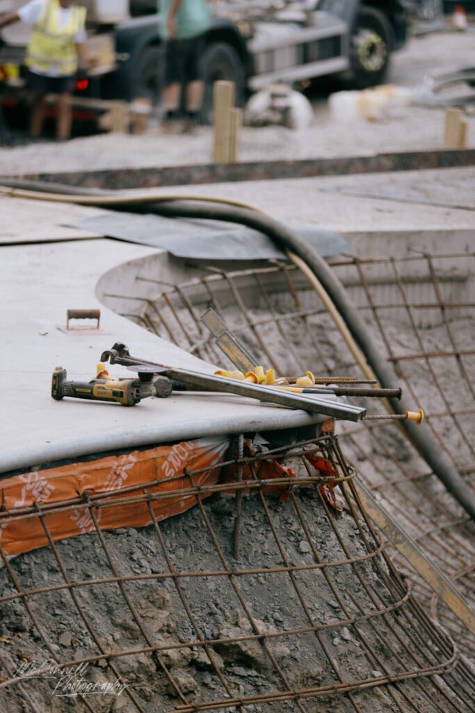 Close-up of construction tools, including a grinder and metal bars, on a partially completed structure with exposed rebar.