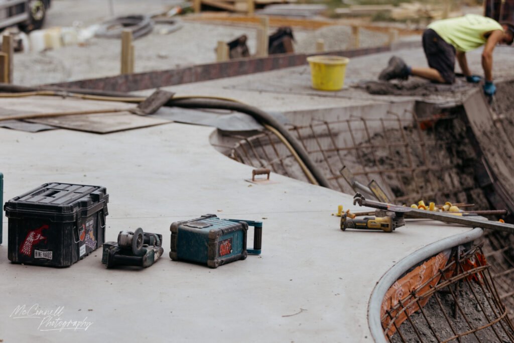 A construction site featuring various tools and equipment, including toolboxes, power tools, and a worker pouring concrete.