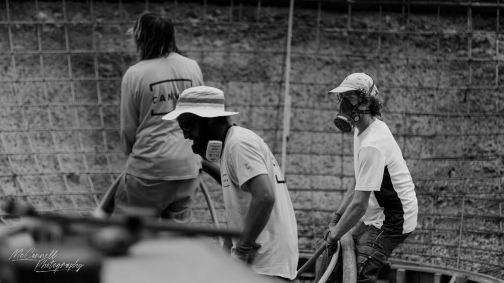Three construction workers wearing safety gear, including masks and hats, engaged in work at a construction site.