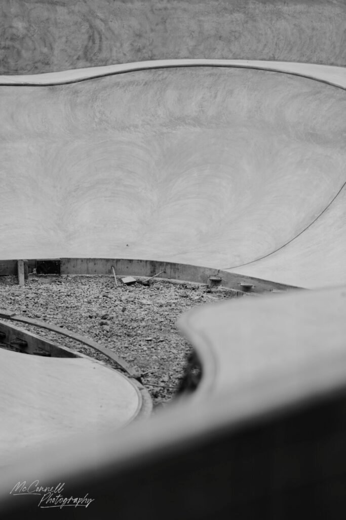A deserted skatepark bowl with smooth, curved surfaces and gravel scattered on the ground.