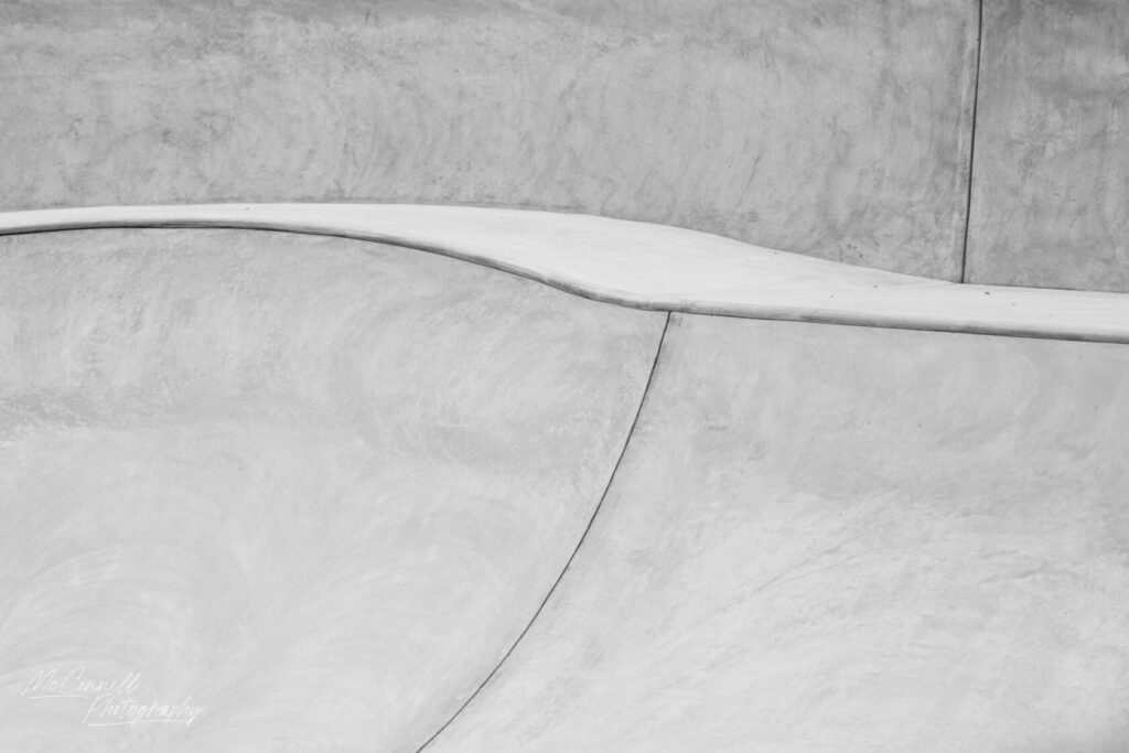 Close-up of smooth concrete curves and lines in a skatepark, rendered in monochrome.