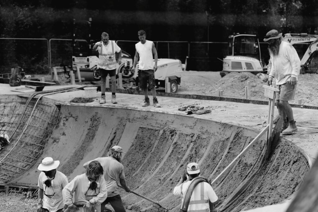 A group of construction workers in a partially completed concrete structure, working on the surface and managing equipment in a construction site.