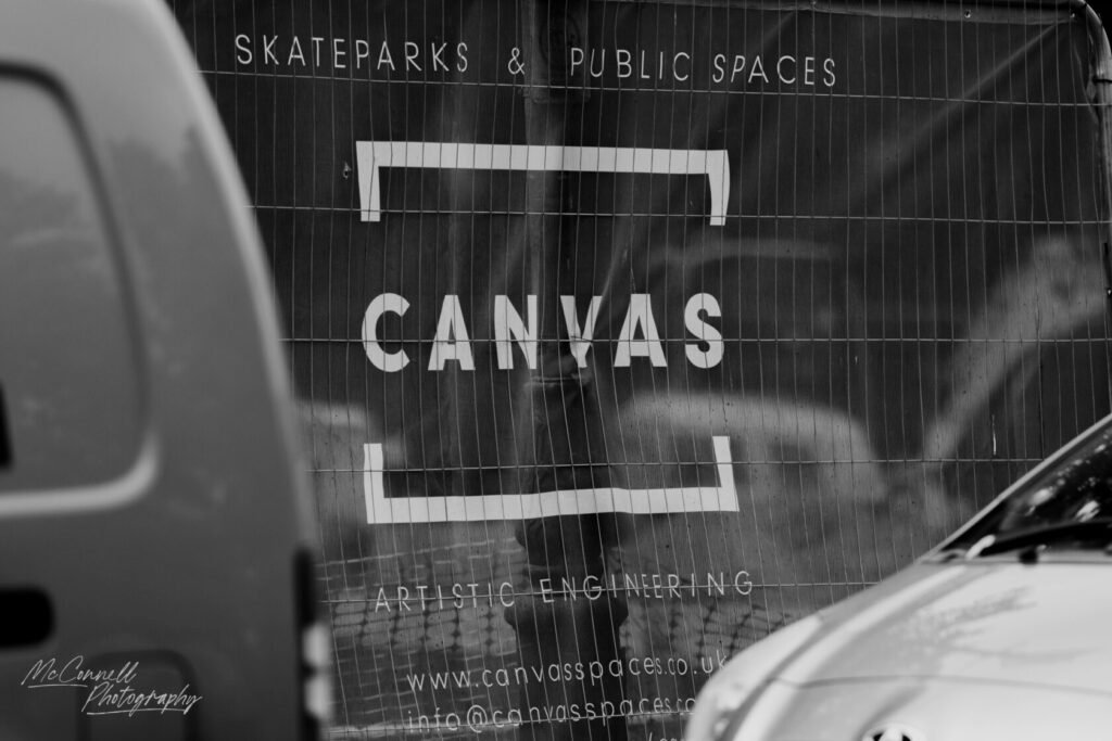 Signage for Canvas, an artistic engineering company, promoting skateparks and public spaces, partially obscured by a vehicle and fencing.