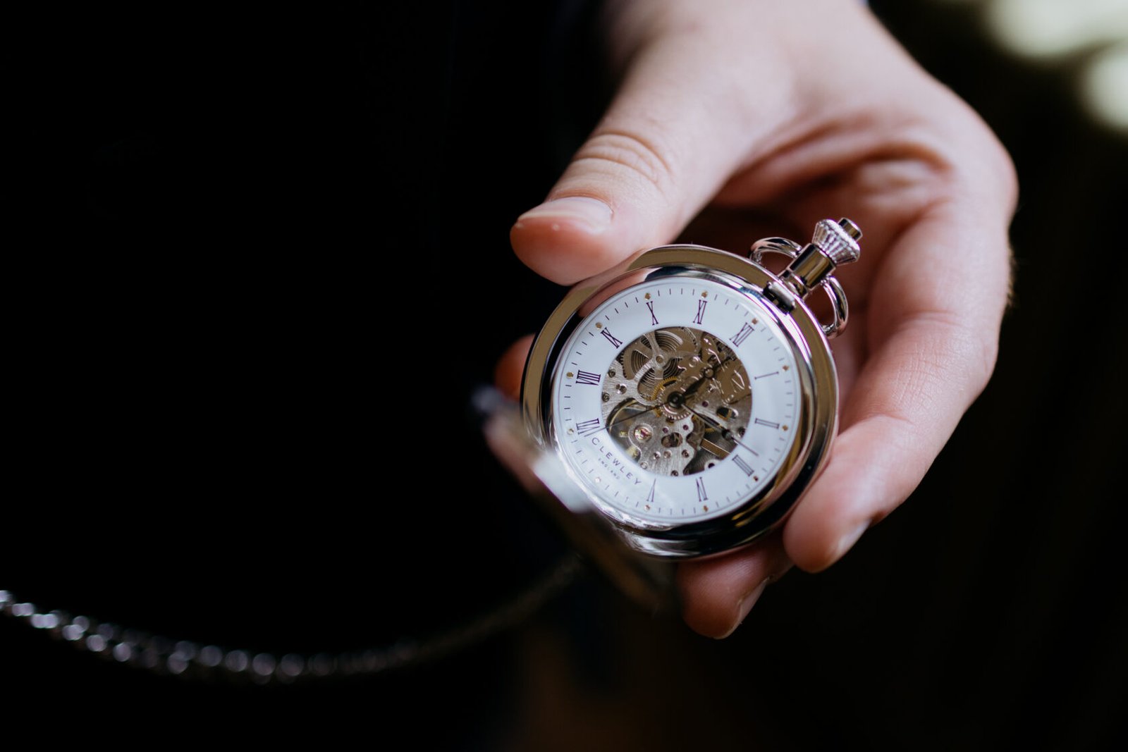 A close-up of an ornate silver pocket watch held in a person's hand, showcasing its intricate inner workings and classic design.