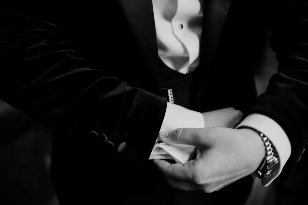 Close-up of a man's hands adjusting his cufflinks while dressed in a formal suit with a velvet jacket.