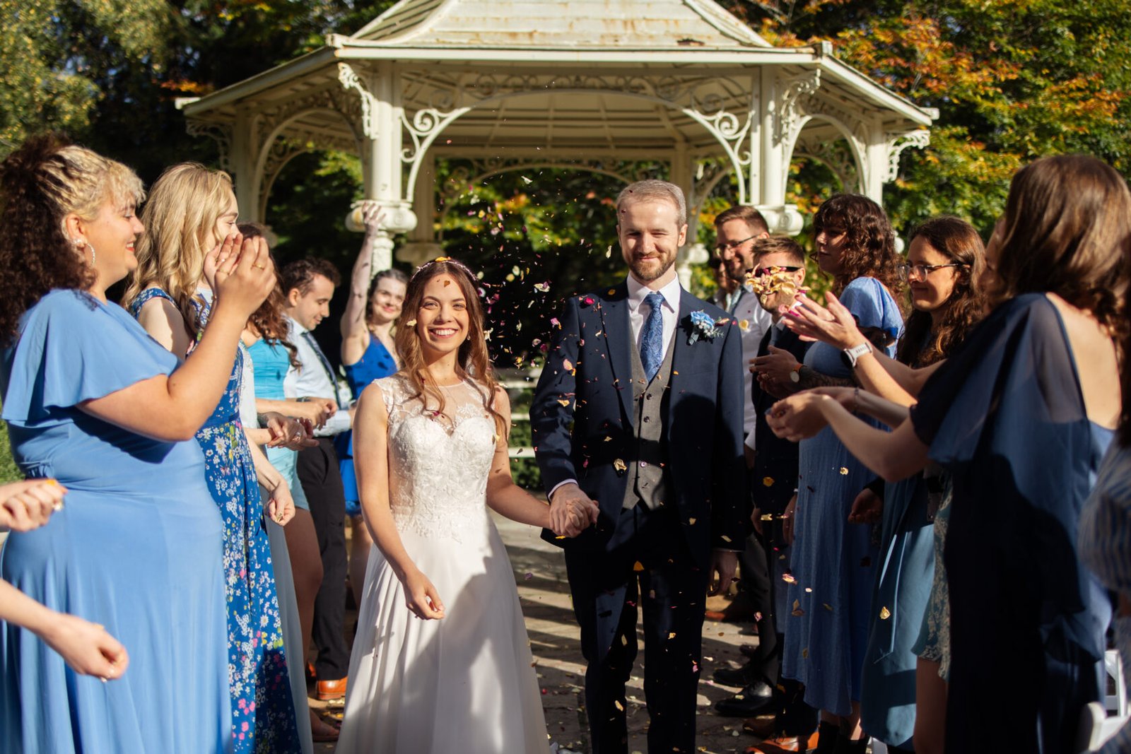 Couple Celebrating with Confetti on Wedding Day A happy couple stands hand in hand during their wedding celebration, surrounded by joyful guests throwing confetti